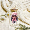 A detailed figurine of a girl with purple skin and dark hair wearing a pink baseball cap and pink outfit is displayed on a wh