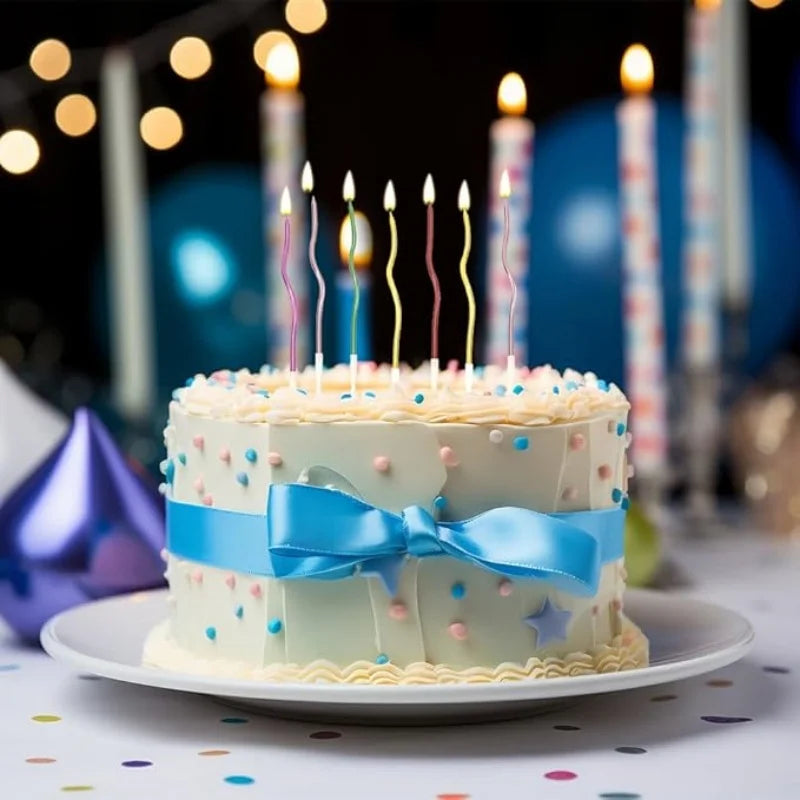 A tiered white birthday cake decorated with colorful sprinkles and blue ribbons, set against a dark background with lit candl