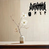 A decorative metal wall-mounted key holder with seven hooks is displayed against a light background with a white flower branc