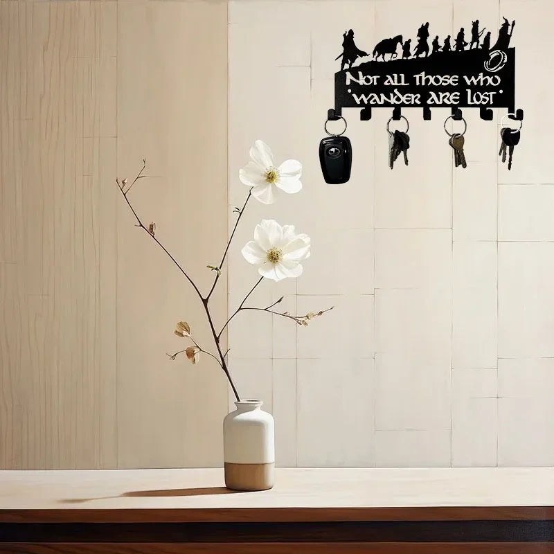 A decorative metal wall-mounted key holder with seven hooks is displayed against a light background with a white flower branc