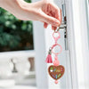 A hand is opening a door, holding a pink silicone bookshelf bead charm with a heart pendant.