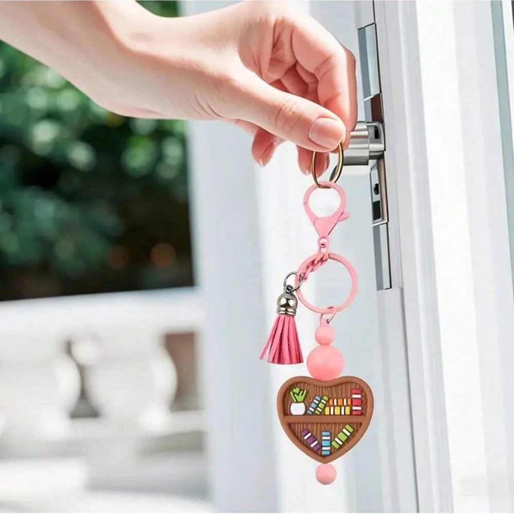 A hand is opening a door, holding a pink silicone bookshelf bead charm with a heart pendant.