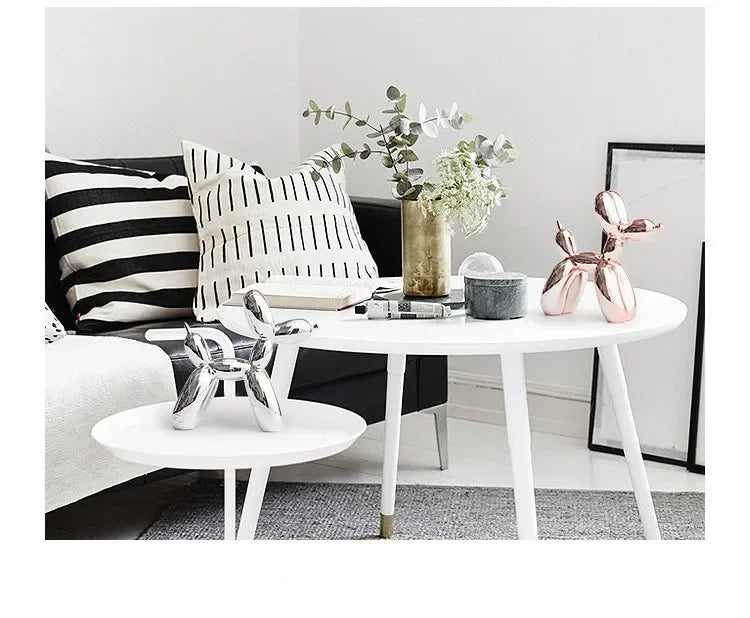 A white table displays a pink resin balloon dog sculpture, greenery, and decorative items in a bright interior setting.