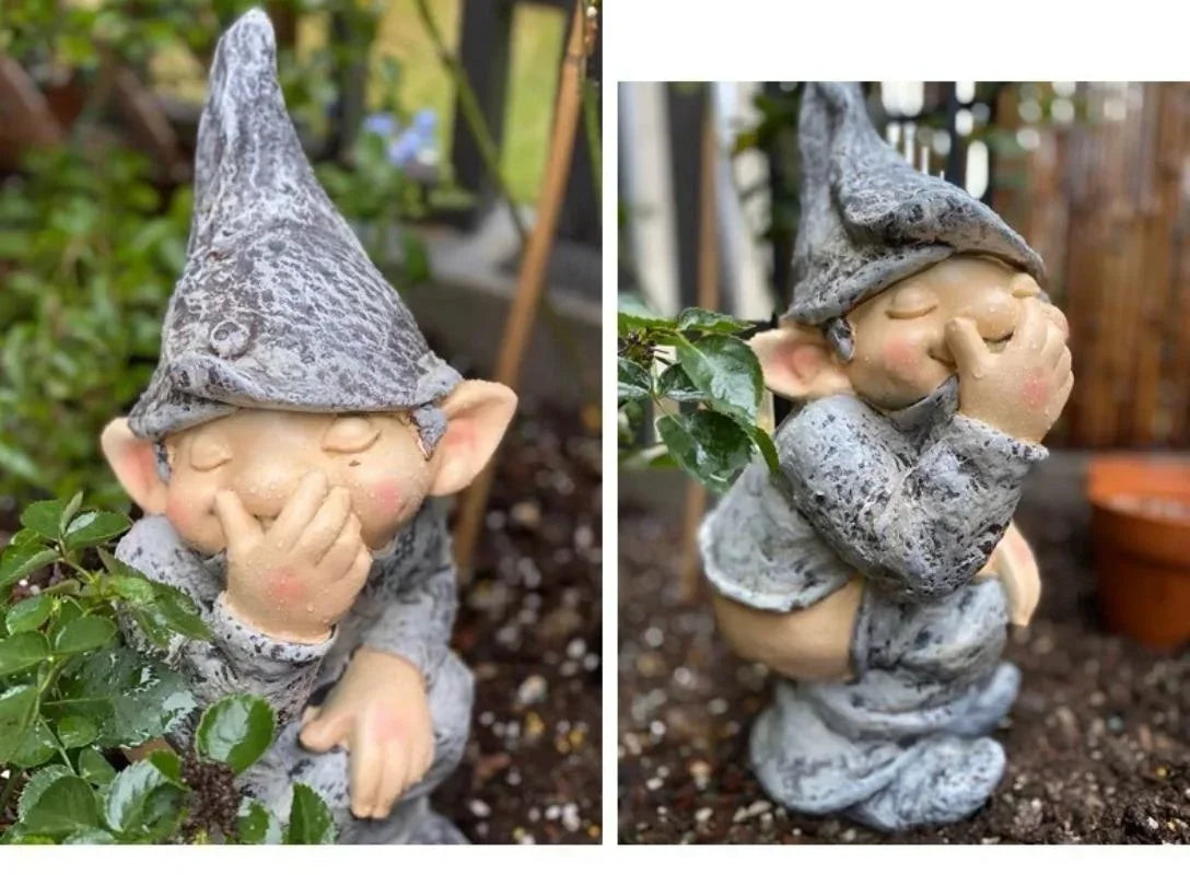A gray gnome statue with a pointed hat and rosy cheeks is nestled among green foliage.