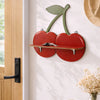 A wooden cherry-shaped wall shelf with a green leaf cutout mounted on a white wall.