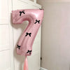 A pink foil balloon shaped like the number 7 with black bows, hanging on a white door.