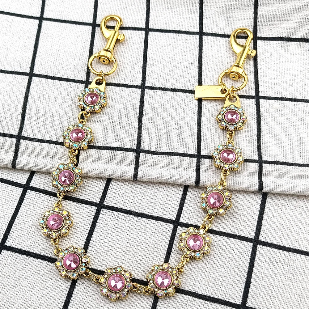 Gold and pink rhinestone bag chain extender with lobster clasps displayed on a white checkered cloth.