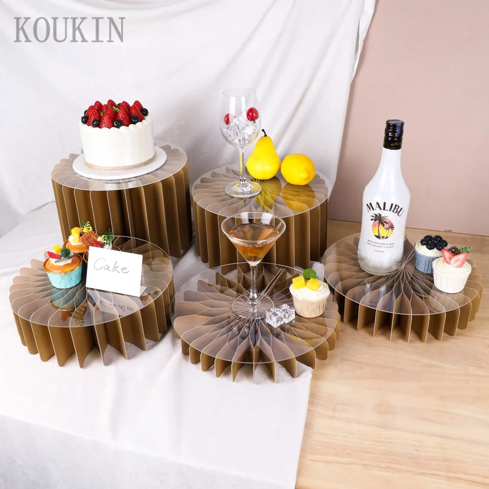 Supports en acrylique pour nourriture présentant un gâteau à la fraise et des fruits jaunes sur une table en bois.