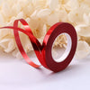 A roll of red satin balloon ribbon is shown against a background of white flowers.