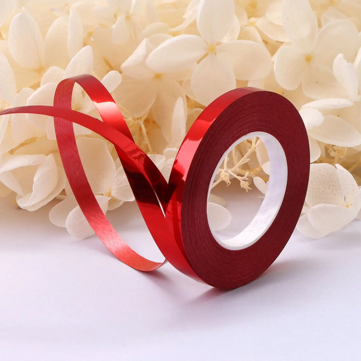 A roll of red satin balloon ribbon is shown against a background of white flowers.