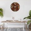 Reloj de pared de madera redondo con esfera blanca y números dorados, colgado en una pared blanca sobre una mesa de madera cl