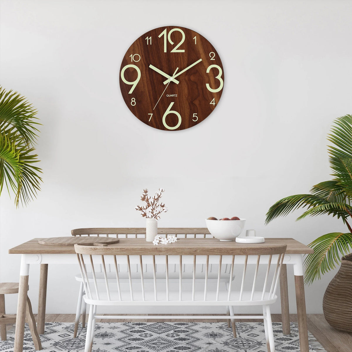 Reloj de pared de madera redondo con esfera blanca y números dorados, colgado en una pared blanca sobre una mesa de madera cl