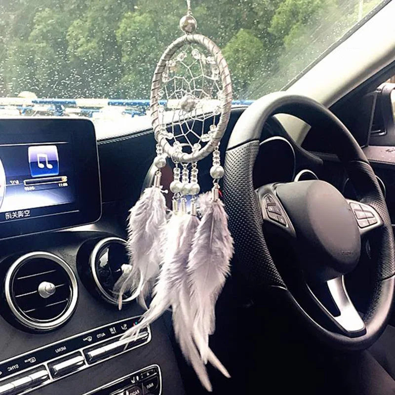 A handmade boho feather dream catcher hanging from the interior of a car, visible near the steering wheel and dashboard.