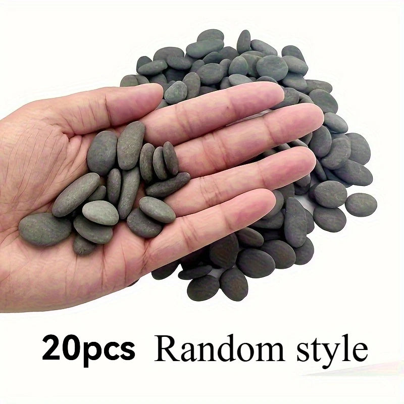A hand holds a pile of 20 smooth, dark gray river rocks for use in aquariums or art projects.