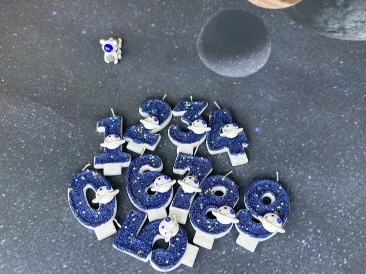 A collection of blue planet-themed birthday candles shaped like numbers 1 through 9, set against a dark gray, starry backgrou