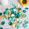 A collection of silk rose petals in various shades of teal, gold, and white scattered on a white checkered cloth.