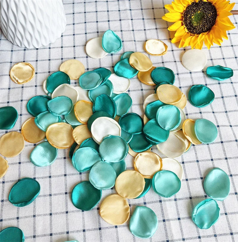 A collection of silk rose petals in various shades of teal, gold, and white scattered on a white checkered cloth.