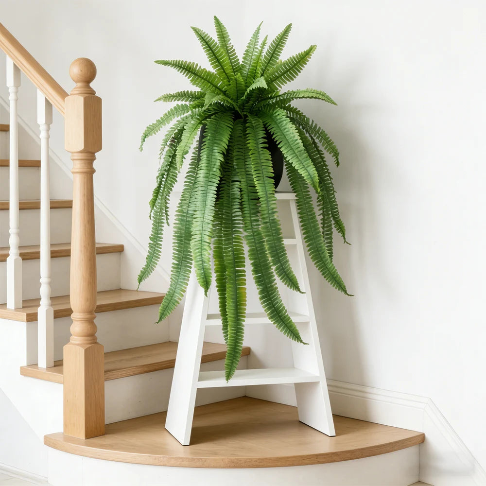 An artificial Persian fern hanging vine in green is displayed on a white wooden ladder next to a staircase.