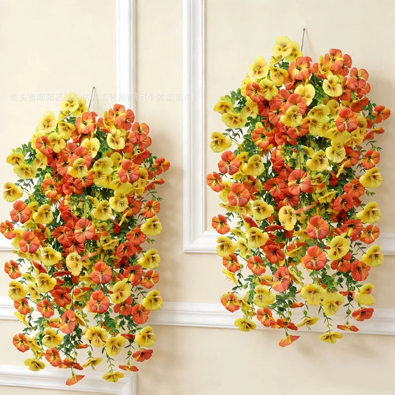A vibrant hanging vine of artificial eucalyptus and violet pansy flowers in shades of orange, yellow, and red.
