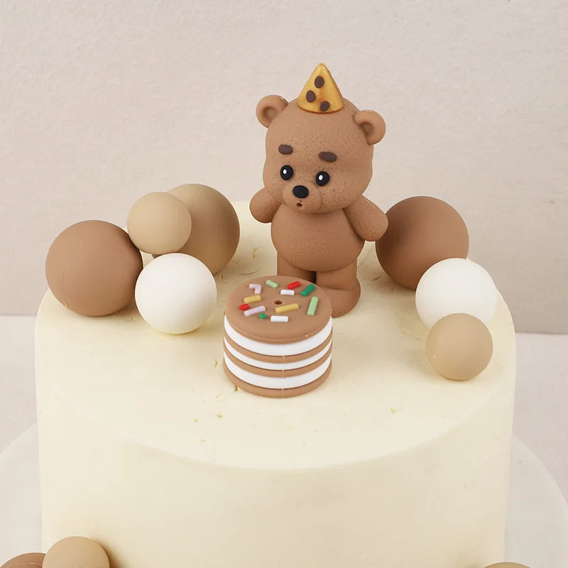 A round cake decorated with a brown teddy bear topper and several round edible decorations.