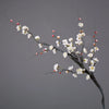 A branch of artificial plum blossoms with white flowers and red buds against a gray background.