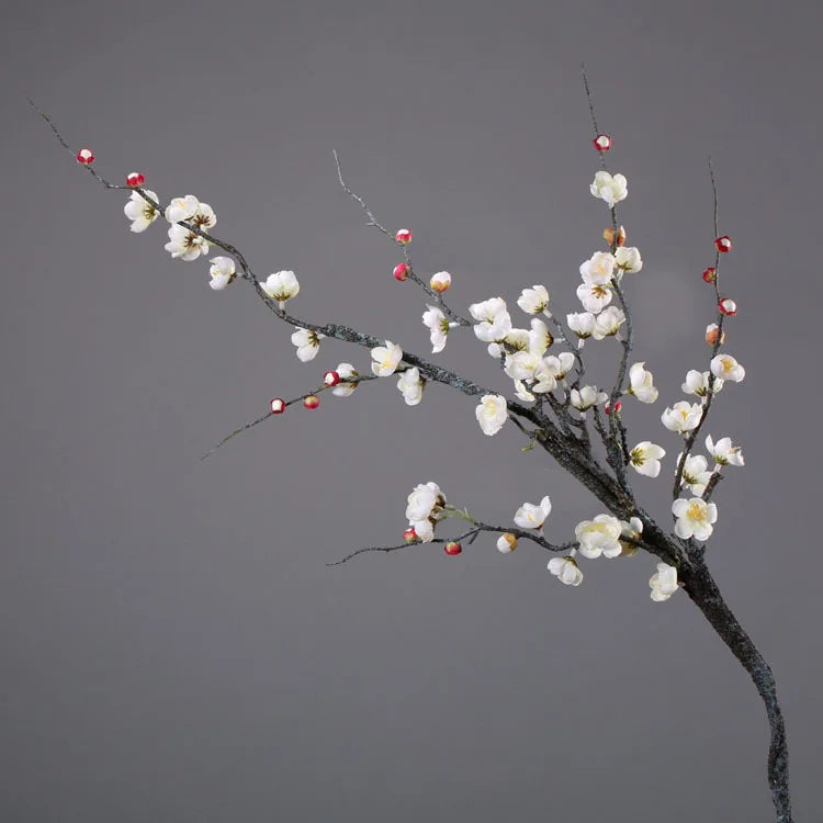 A branch of artificial plum blossoms with white flowers and red buds against a gray background.