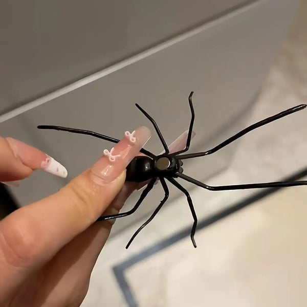 A hand holds a black realistic spider magnet with white accents against a light background.