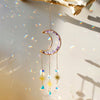A delicate gold moon-shaped crystal pendant hangs against a bright background with rainbow light refractions.
