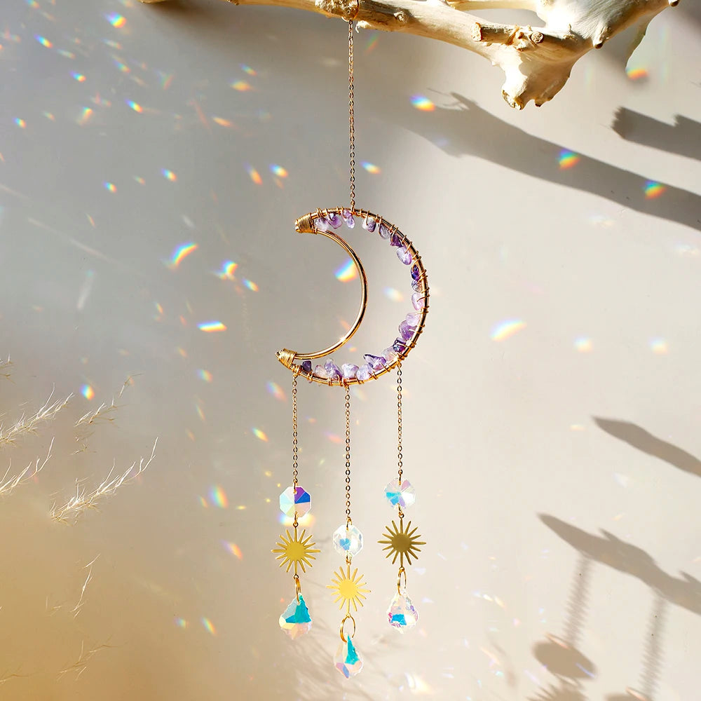 A delicate gold moon-shaped crystal pendant hangs against a bright background with rainbow light refractions.