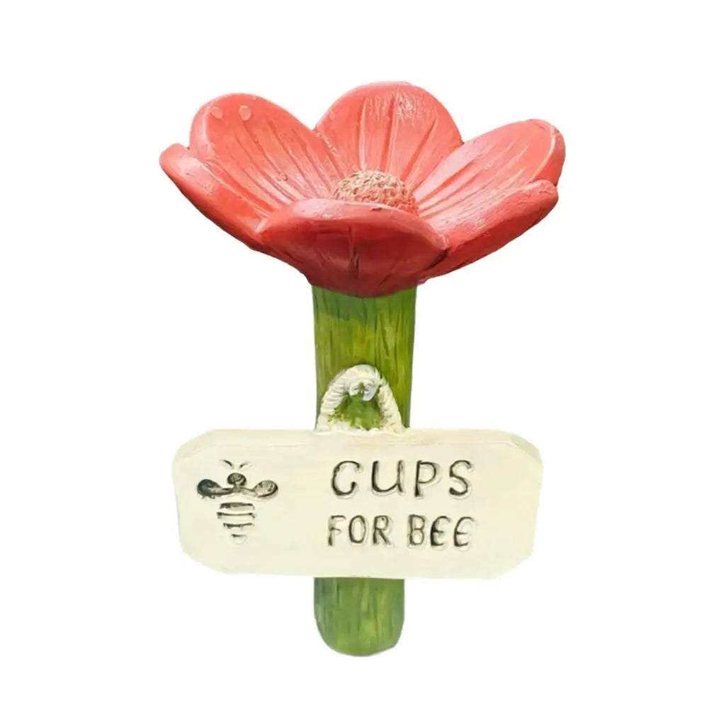 A red flower with a yellow center is mounted on a green stem, featuring a tag that reads GUPS FOR BEE.