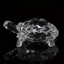 Un ornamento de tortuga de cristal transparente reflejándose en una superficie oscura.