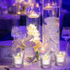 A collection of clear glass cylinders filled with floating candles and white flowers on a table.