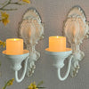A set of two vintage wrought iron wall-mounted candle holders with white wax candles.