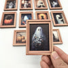 A hand holds a framed print featuring a ghostly figure against a dark background, part of a Halloween decor set.
