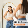 A woman is looking at her reflection in a full length arched wall mirror.