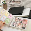 A hand holds a clear plastic binder filled with K-Pop photo cards and a black binder.