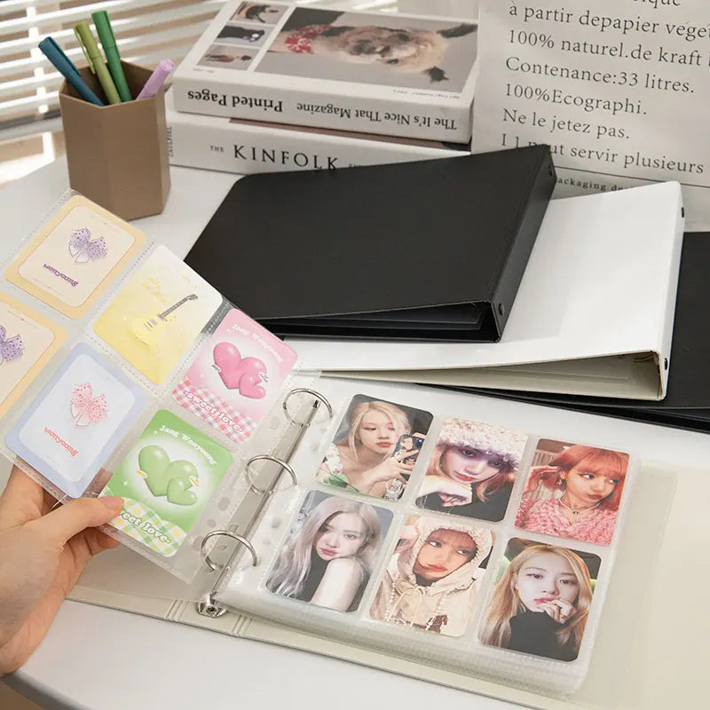A hand holds a clear plastic binder filled with K-Pop photo cards and a black binder.