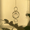 Une délicate chaîne en or avec un pendentif de cristal clair à anneaux concentriques contre un mur ensoleillé.