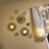 A set of three gold sunflower wall mirrors mounted on a beige wall next to a sheer white curtain.