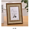 A rectangular wooden photo frame with a distressed finish displaying the text Home is Where the Is and a silhouette of a shoe