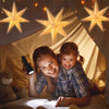 A smiling girl and woman are sitting inside a tent surrounded by glowing star pendant lights.