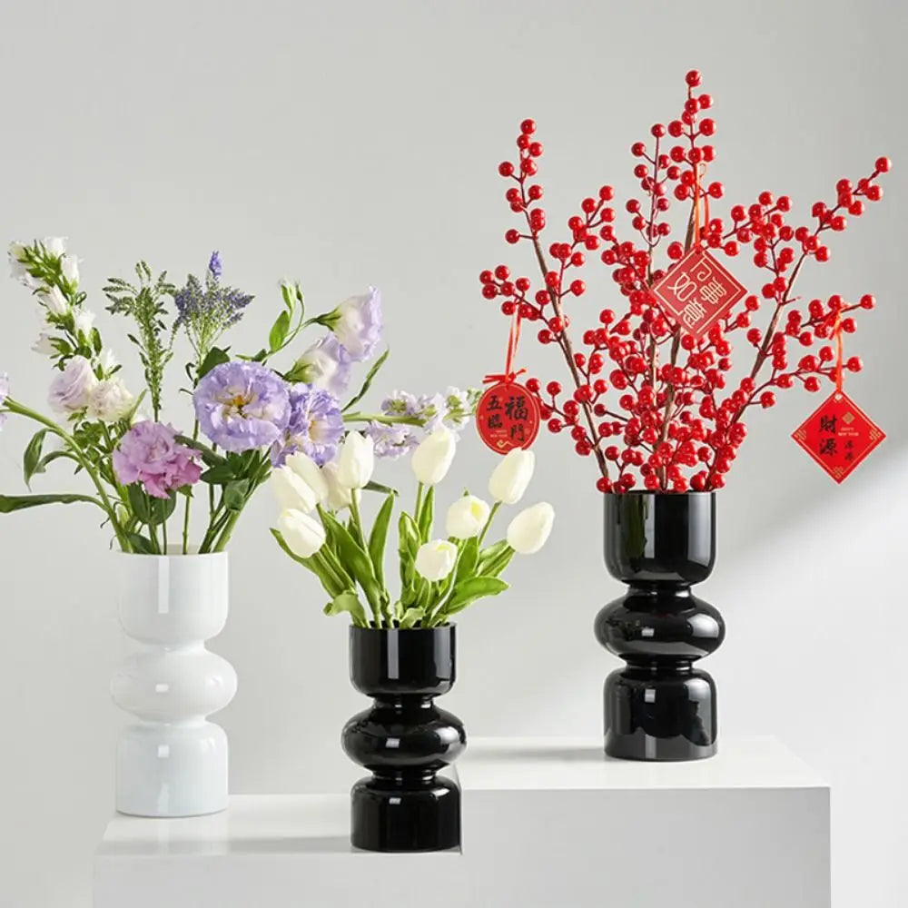A black ceramic vase holds vibrant red berries and green foliage, used as a decorative arrangement.
