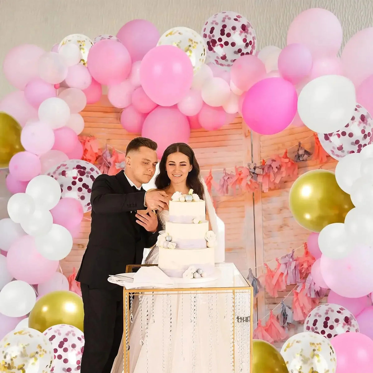 A pink and gold balloon arch decoration featuring latex balloons and confetti in a wedding or celebration setting.