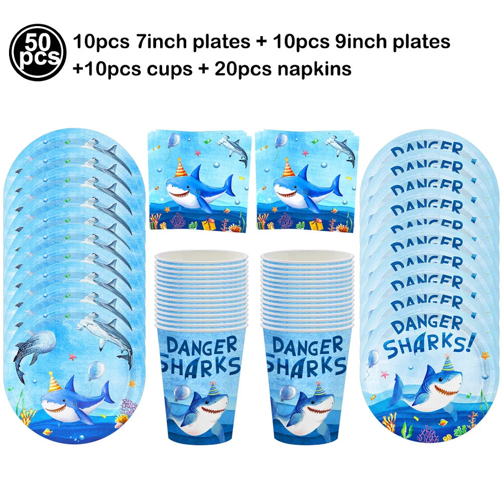 A set of blue shark themed party supplies including plates, cups, and napkins.