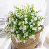 A vibrant green faux eucalyptus branch with white flowers in a woven basket for home decor