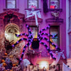 A decorative Halloween spider web light installation featuring purple LED strands and ghostly figures in a pink facade.