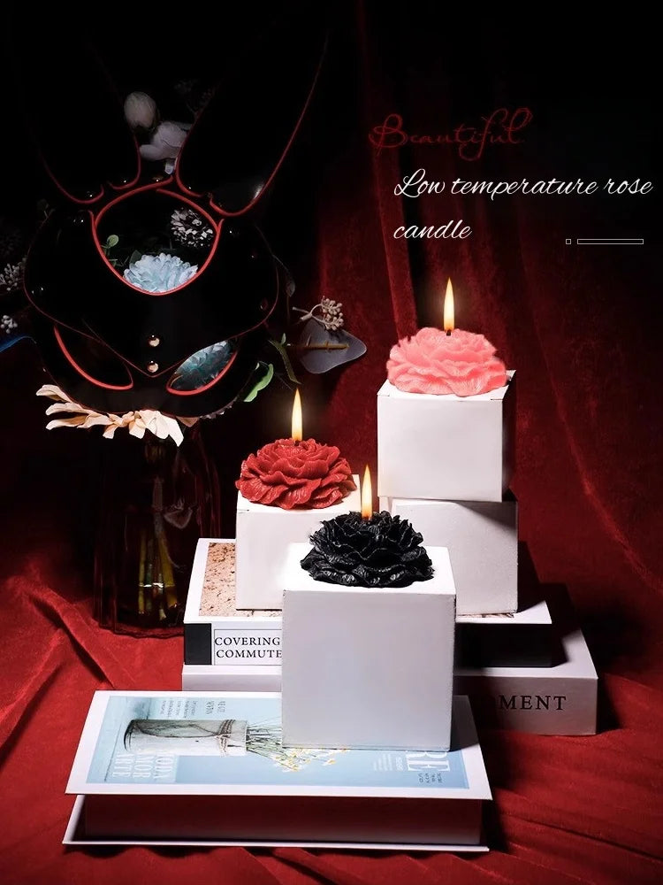 A display featuring a beautiful low temperature rose candle surrounded by dark floral elements and stacked white boxes.