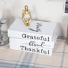 A set of three modern decorative fake books in white with gold script text and a golden figure on top.