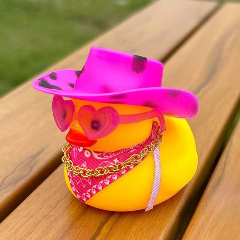 A rubber duck shaped like a cowboy hat with pink and black patterns, wearing an orange heart necklace, sitting on a wooden su