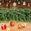 A realistic cedar garland with flexible branch design decorated with Christmas ornaments and wrapped gifts on a wooden surfac